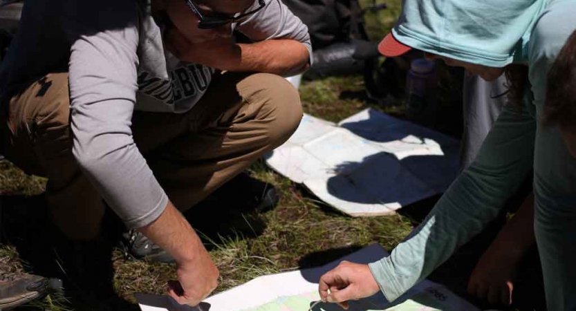 teens point to a map while navigating a backpacking expedition